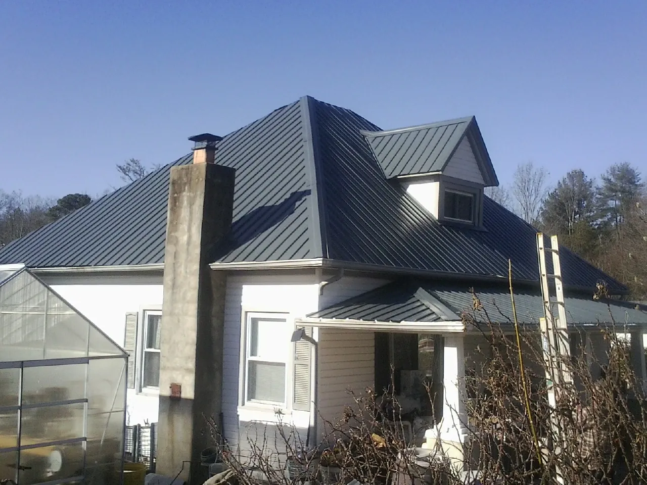 Dark blue standing seam metal roof on a white farmhouse with dormer — Slate & Tile Roof Repair by Roofing Brothers in Kew Gardens