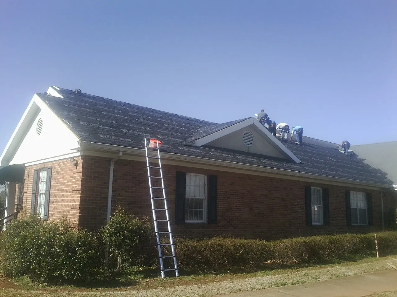 Crew tearing shingles off a brick ranch roof with a ladder set — Metal Roof Repair work by our crew in Kew Gardens