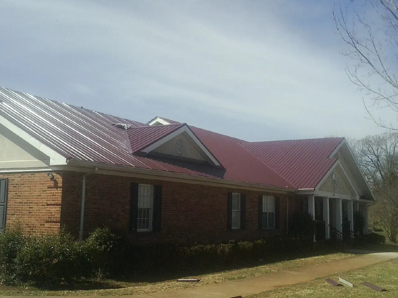 Red metal roof with gabled entries on a long brick building, from a Hail Damage Roof Repair job in Kew Gardens