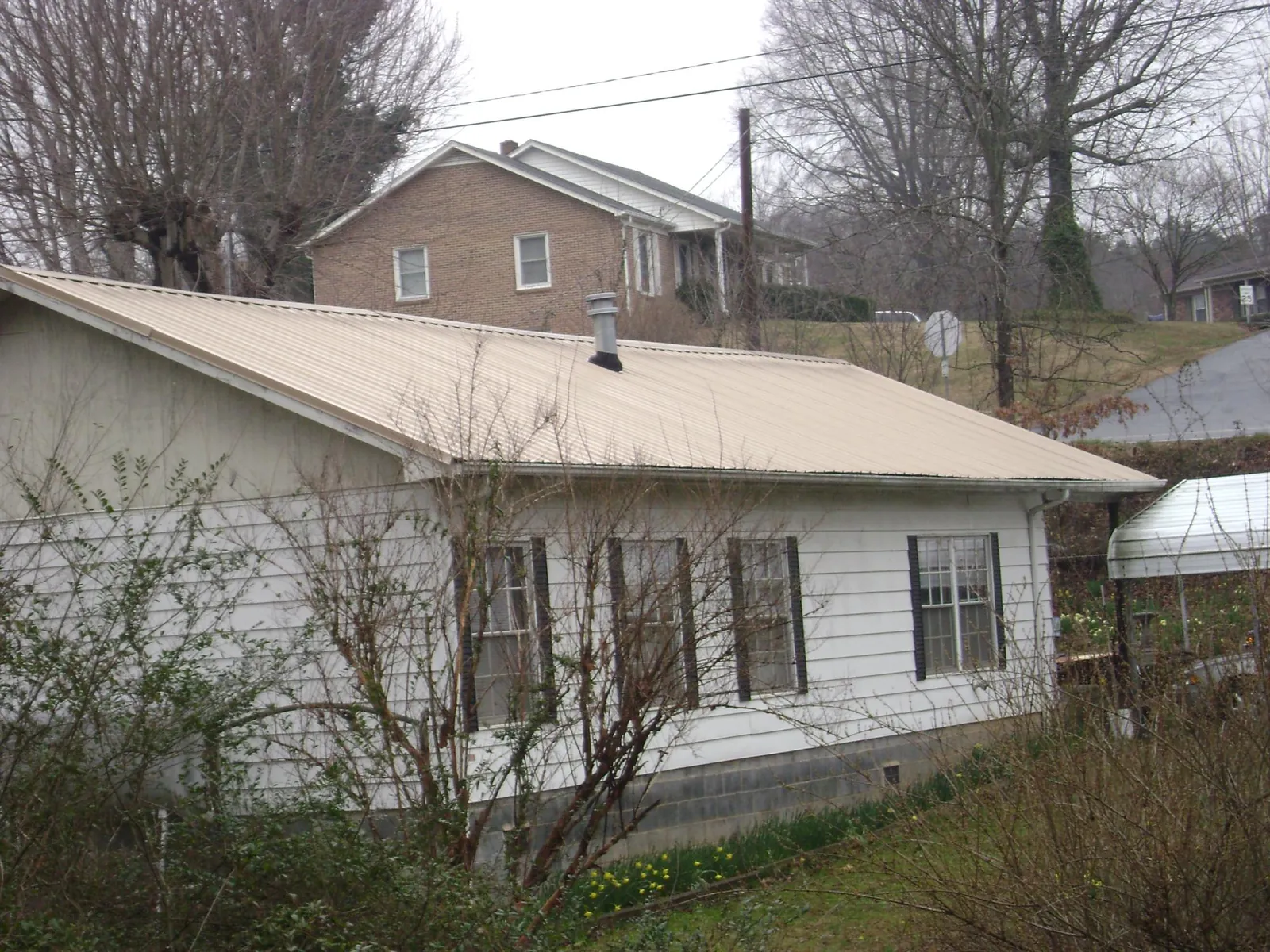 Tan metal roof on a white sided house set into a hillside — Commercial Roofing by Roofing Brothers in Kew Gardens