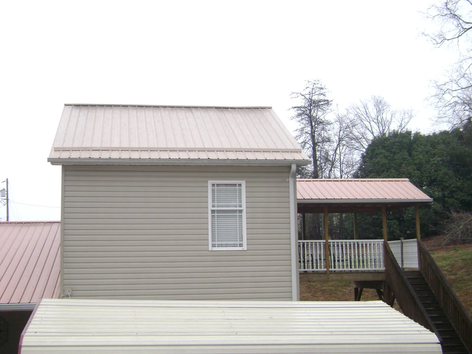 Tan metal roofs on a two story addition and attached porch, from a Roof Replacement job in Kew Gardens